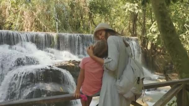 Una joven madre y su linda hija descansando contra la cascada de una cascada — Vídeo de stock