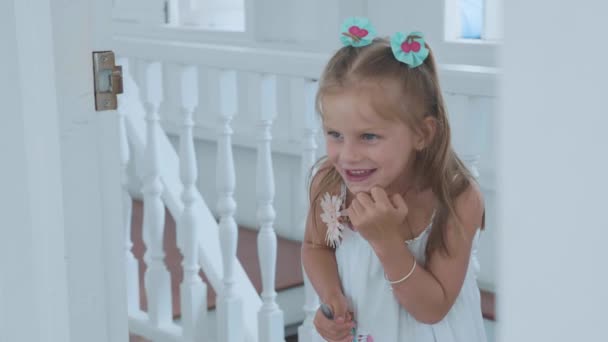 Маленька мила дівчинка дивиться через двері в кімнаті з кумедними емоціями — стокове відео