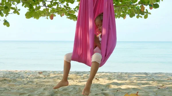 Niña linda haciendo ejercicios de yoga con hamaca en la playa . — Foto de Stock