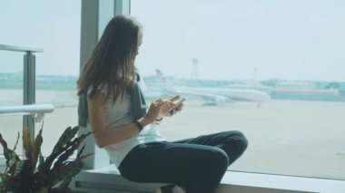 Genç kadın havaalanında uçak arka planda ile akıllı telefon kullanıyor