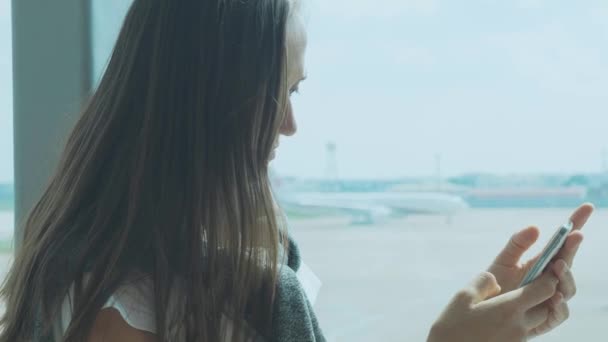 Mujer joven está utilizando el teléfono inteligente en el aeropuerto con avión en el fondo — Vídeos de Stock