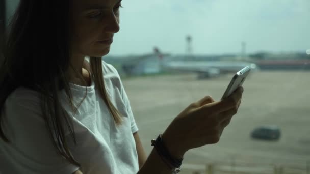 Jeune femme utilise un téléphone intelligent à l'aéroport avec avion en arrière-plan 