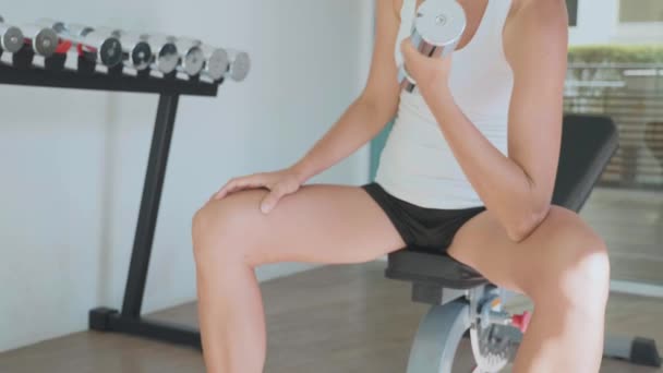 Ung kvinna sitter på bänken och gör biceps övning av hantel i idrottsförening. — Stockvideo
