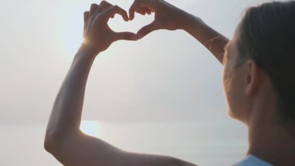 Mani femminili che fanno gesto a forma di cuore tenendo il sole bagliore — Video Stock