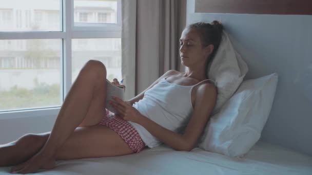 Jonge vrouw liggend op het bed en 's morgens pagina's schrijven in dagboek, slow-motion — Stockvideo