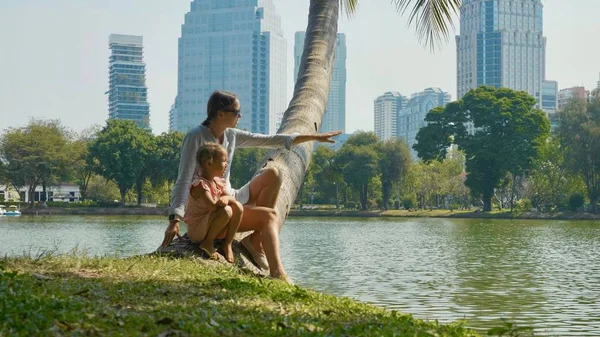 Família relaxante no parque com lago e arranha-céus em segundo plano — Fotografia de Stock