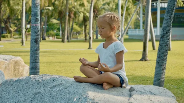 Malé dítě dívka meditoval v krásném parku s palmami v pozadí — Stock fotografie