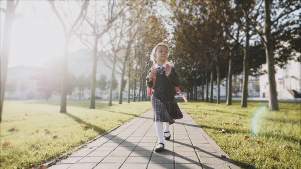 Menina jovem em uniforme escolar está andando no parque em tempo ensolarado . — Fotografia de Stock