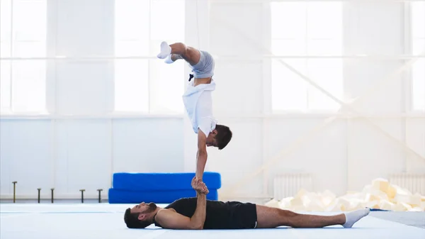 Fit muž a teenager praktikující akrobatickou ruční stánku v tělocvičně. — Stock fotografie