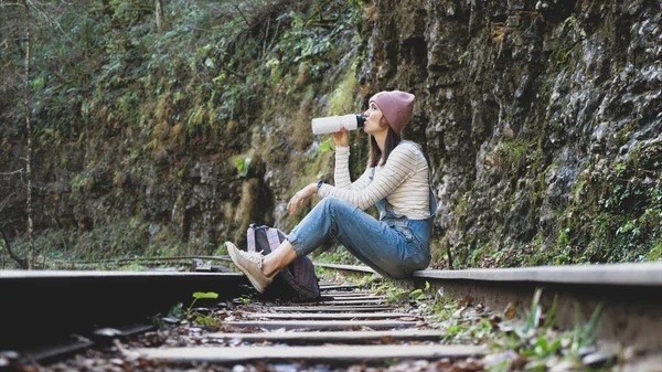 Joven mochilero mujer está sentado en tren ferrocarril y agua potable — Foto de Stock