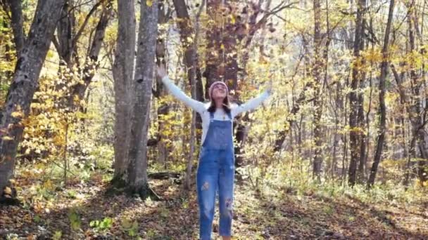 Mujer joven feliz divirtiéndose y lanzando hojas amarillas en el bosque de otoño — Vídeos de Stock