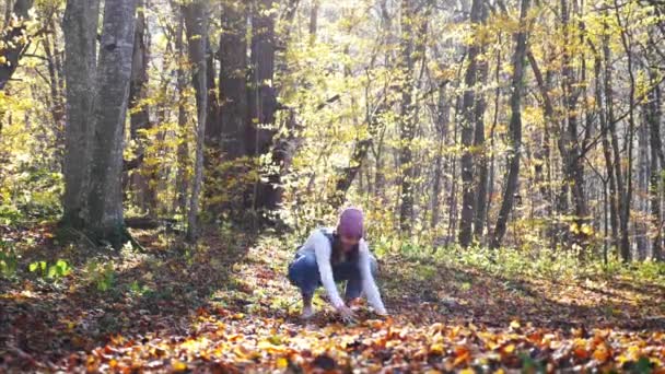 Счастливая молодая женщина веселится и бросает желтые листья в осенний лес — стоковое видео