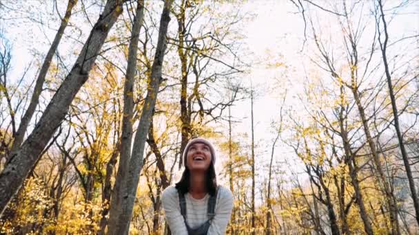 Mujer joven feliz divirtiéndose y lanzando hojas amarillas en el bosque de otoño — Vídeos de Stock
