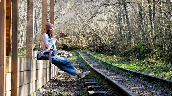 Mulher mochileiro jovem está sentado na estação ferroviária e usando smartphone — Fotografia de Stock