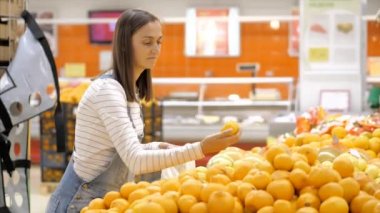 Kot pantolon giymiş genç bir kadın marketten taze portakal seçiyor..