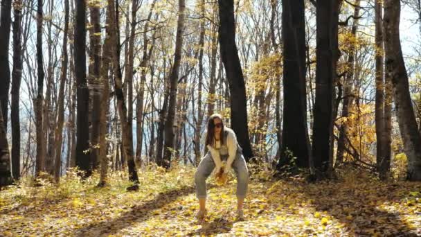 Щаслива молода жінка розважається і кидає жовте листя в осінній ліс — стокове відео