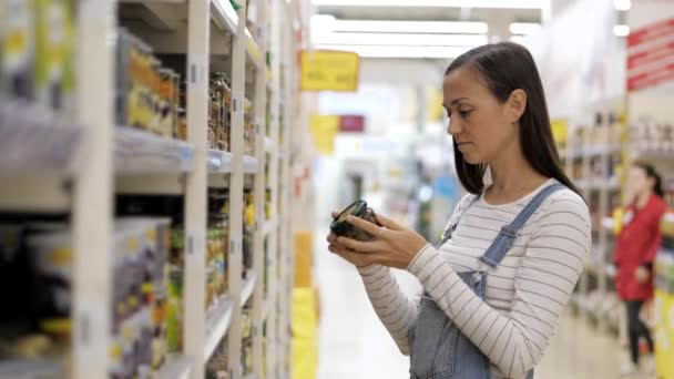 Молода жінка вибирає консервовані гриби в скляній банці в супермаркеті . — стокове відео