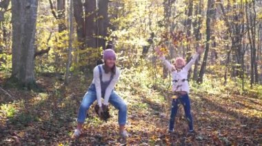 Mutlu genç kadın sonbahar ormanında eğleniyor ve sarı yapraklar fırlatıyor.