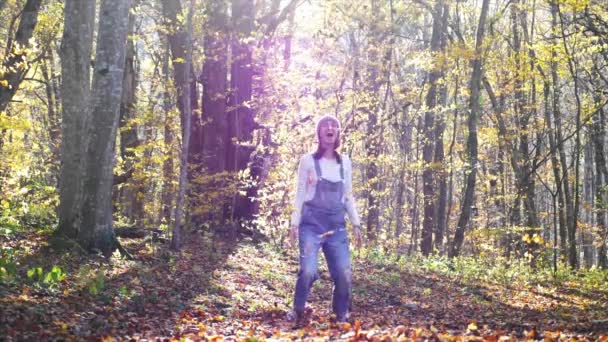 Szczęśliwa młoda kobieta bawiąca się i rzucająca żółtymi liśćmi w jesiennym lesie — Wideo stockowe