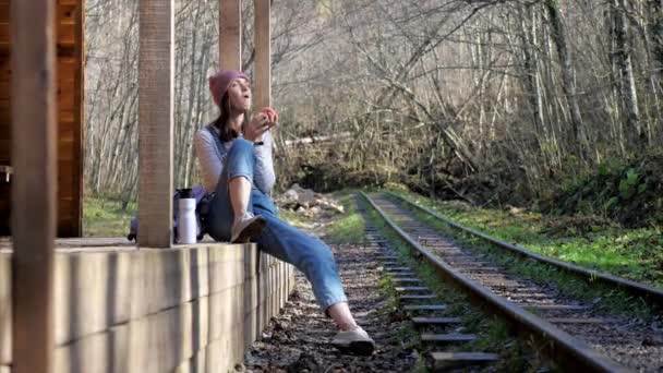 Молодая женщина-турист сидит на вокзале и ест яблоко — стоковое видео