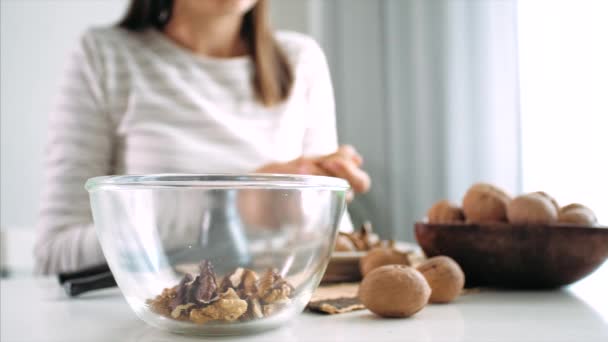 Young woman is cracking a walnuts and collecting it in glass bowl, close-up — Stockvideo
