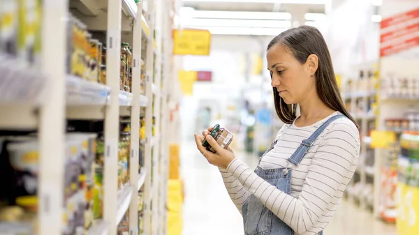 Genç kadın süpermarkette cam kavanozda konserve mantar seçiyor..