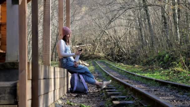 Młoda Backpacker kobieta siedzi na stacji kolejowej i wody pitnej — Wideo stockowe