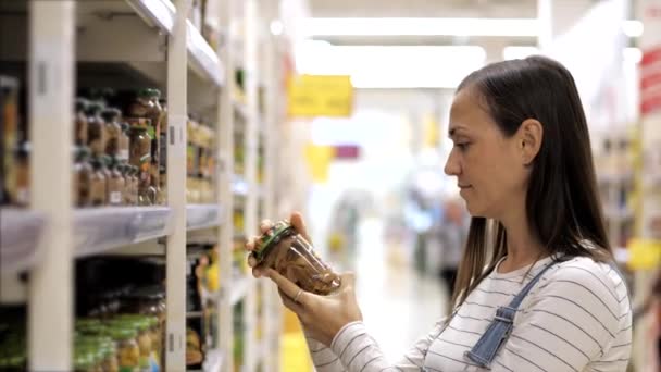 Wanita muda adalah memilih jamur kalengan dalam botol kaca di supermarket . — Stok Video