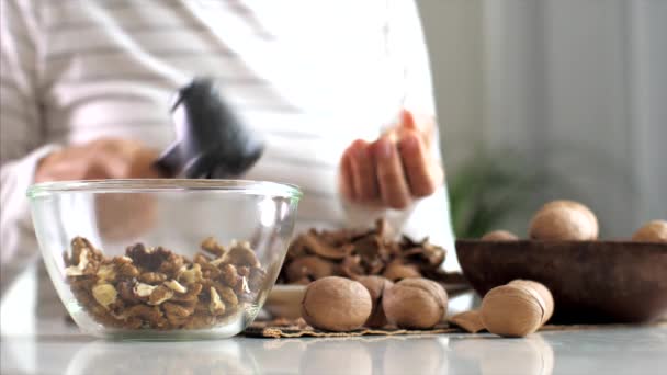 Young woman is cracking a walnuts and collecting it in glass bowl, close-up — Stockvideo