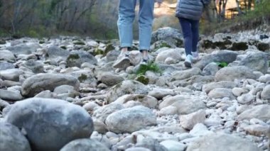 Küçük kızı olan genç anne dağ nehrinin kıyısında yürüyor.