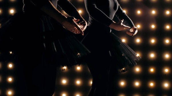 Silhouette of two ballerinas in black tutu is dancing ballet in the dark studio.