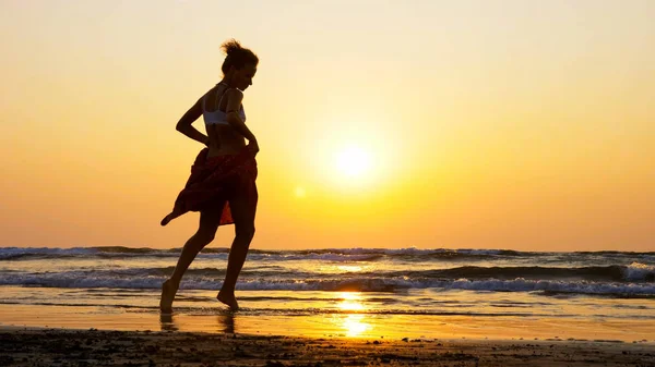 Силуэт молодой девушки, танцующей на пляже на закате — стоковое фото