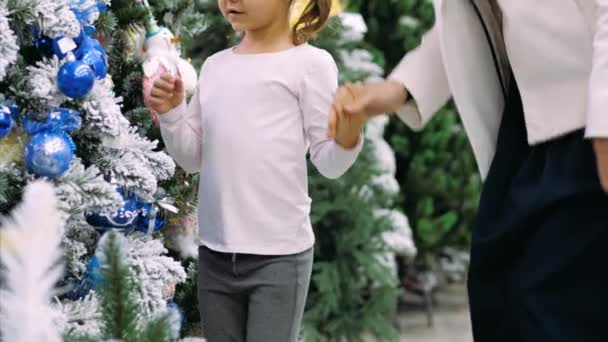 Junge Mutter und kleine Tochter suchen sich Weihnachtsbaum im Laden aus. — Stockvideo
