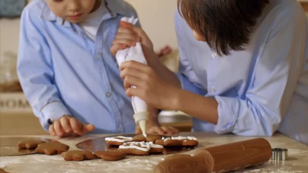 Due fratelli stanno decorando un biscotto natalizio con sacchetto di pasticceria in cucina a casa . — Video Stock