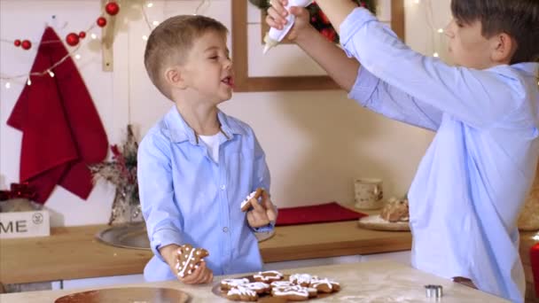 Two brothers is decorating a Christmas cookies with pastry bag at home kitchen. — 비디오