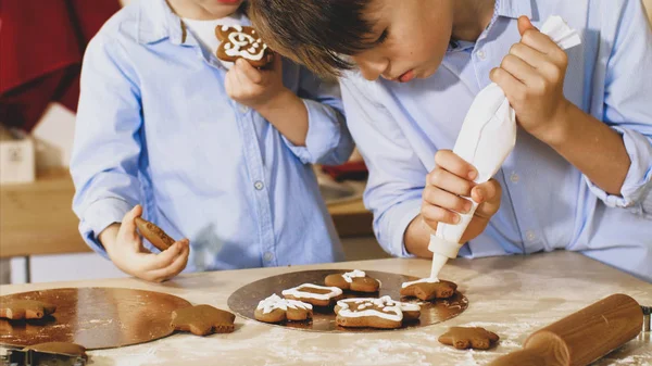 Два брати прикрашають різдвяне печиво кондитерською сумкою на домашній кухні . — стокове фото