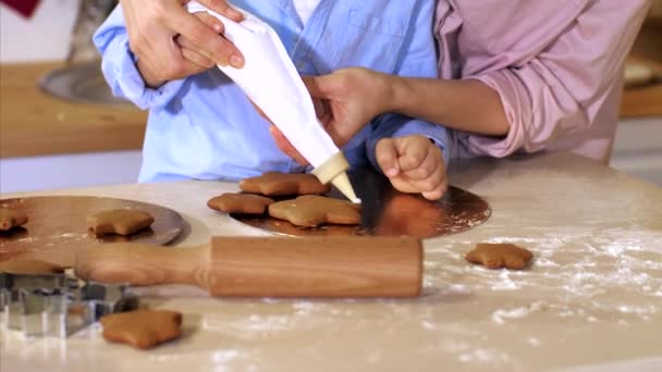 Mère avec fils est décore un biscuits de pain d'épice de Noël avec sac à pâtisserie — Video