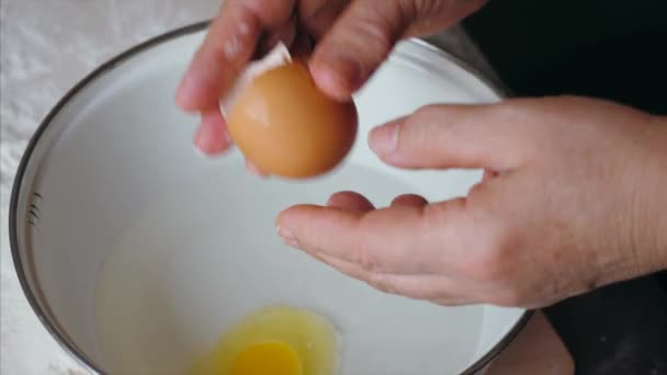 Mature woman cracking the egg in steel bowl with water for preparing a dough — Stock Video