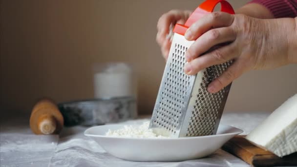 Close-up hands of mature woman is rubs a cheese on a steel grater — Stock Video