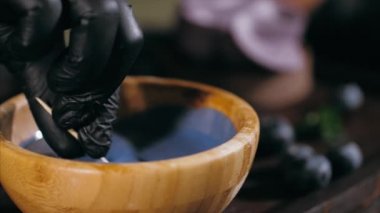 Pastry chef is dips a candy in caramel for topping a blueberry cake, close-up