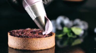 Pastry chef decorates biscuit with purple cream from pastry bag, close-up.