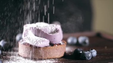Pastry chef is sprinkles a cake with powdered sugar in slow motion, close-up.