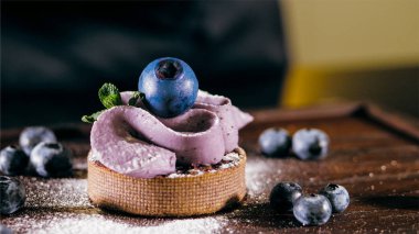 Cake with purple cream on the table near the blueberries, close-up.