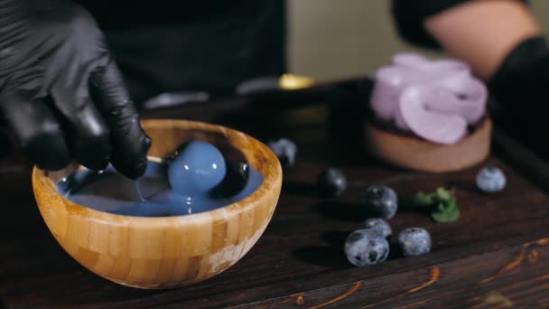 Pastry chef is dips a candy in caramel for topping a blueberry cake, close-up — Stock Video