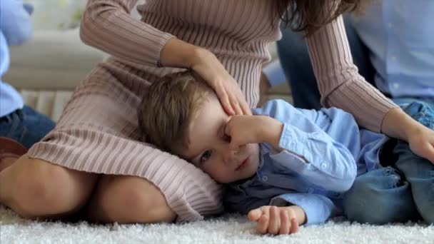 Pequeño hijo está acostado en las rodillas de las madres, en el suelo mientras mamá lo acaricia — Vídeos de Stock