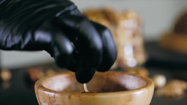 Pastry chef is dips a hazelnut in caramel for making topping for a cake — Stok video