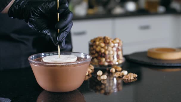 Pastry chef is dips a candy in liquid chocolate with nuts for making a cake — 비디오