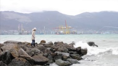 Woman is walking by empty seafront in windy weather with crashing sea waves