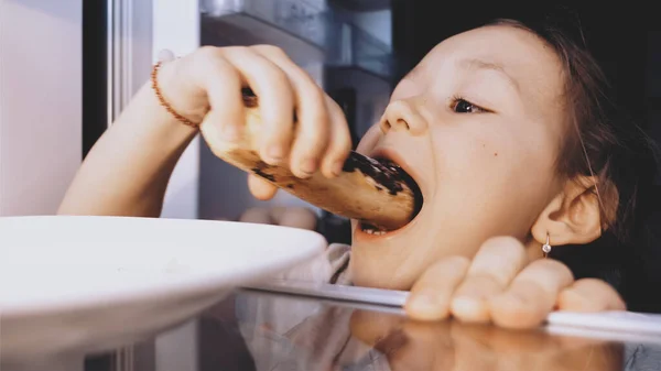 Дитяча дівчинка відкриває холодильник, приймає клерка і їсть його густо . — стокове фото