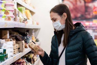 Tıp maskeli genç bir kadın süpermarketten mandıra alıyor.